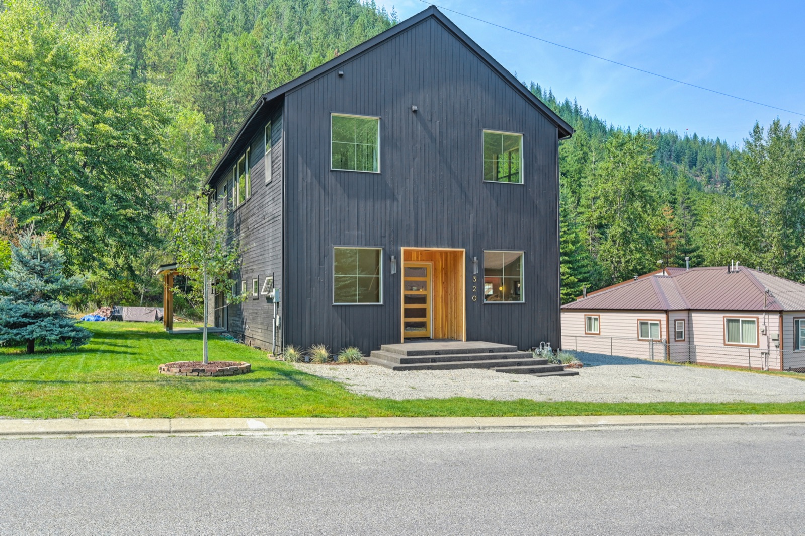 Modern black board-and-batten custom home with a cedar entry against a forested mountainside in the Silver Valley